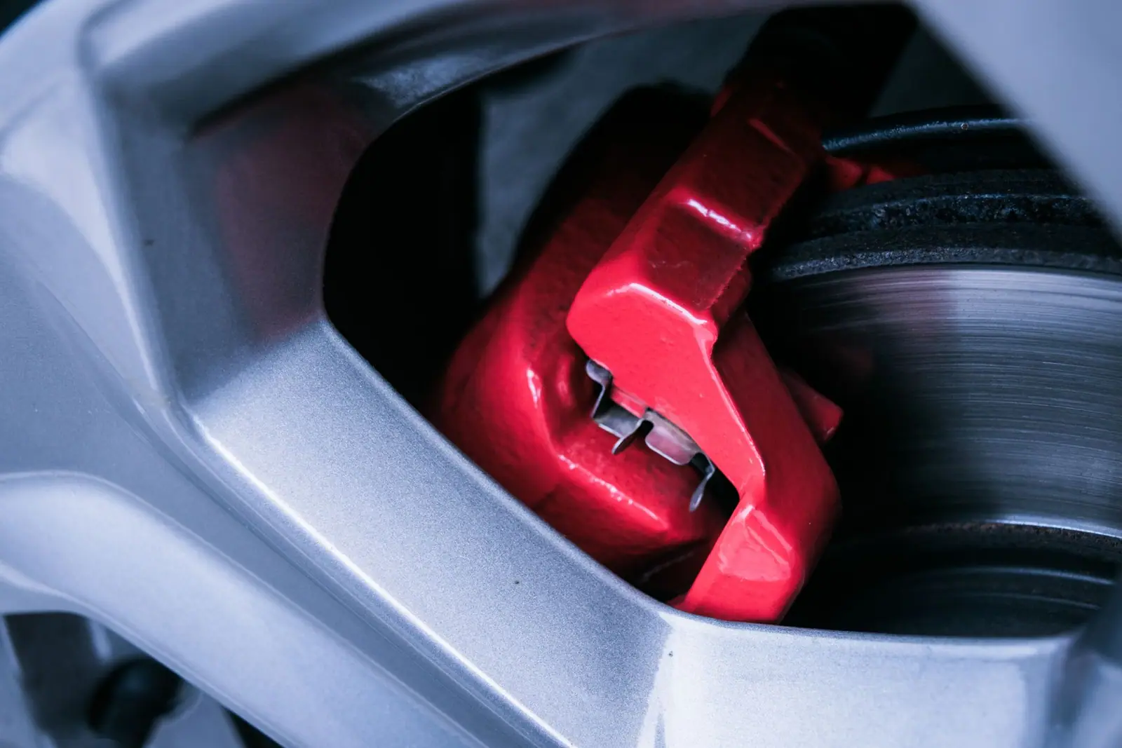 A red brake caliper visible through a wheel beside a brake rotor