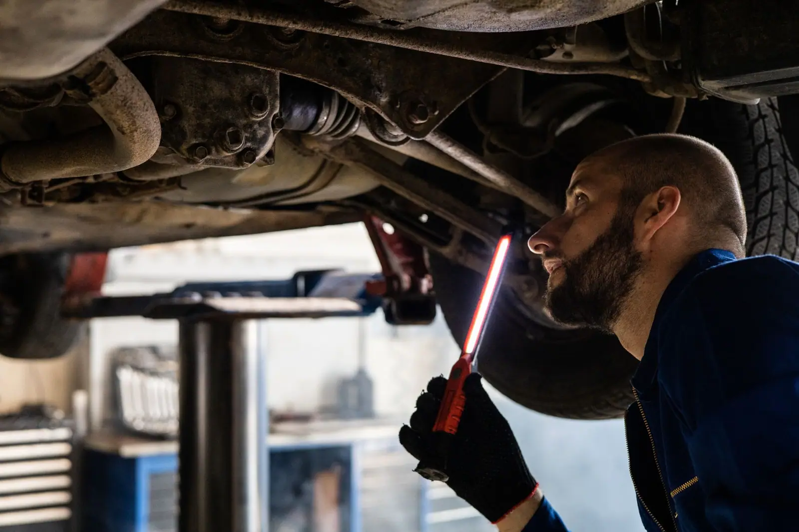 A mechanic holding a light while inspecting a raised vehicle's underside