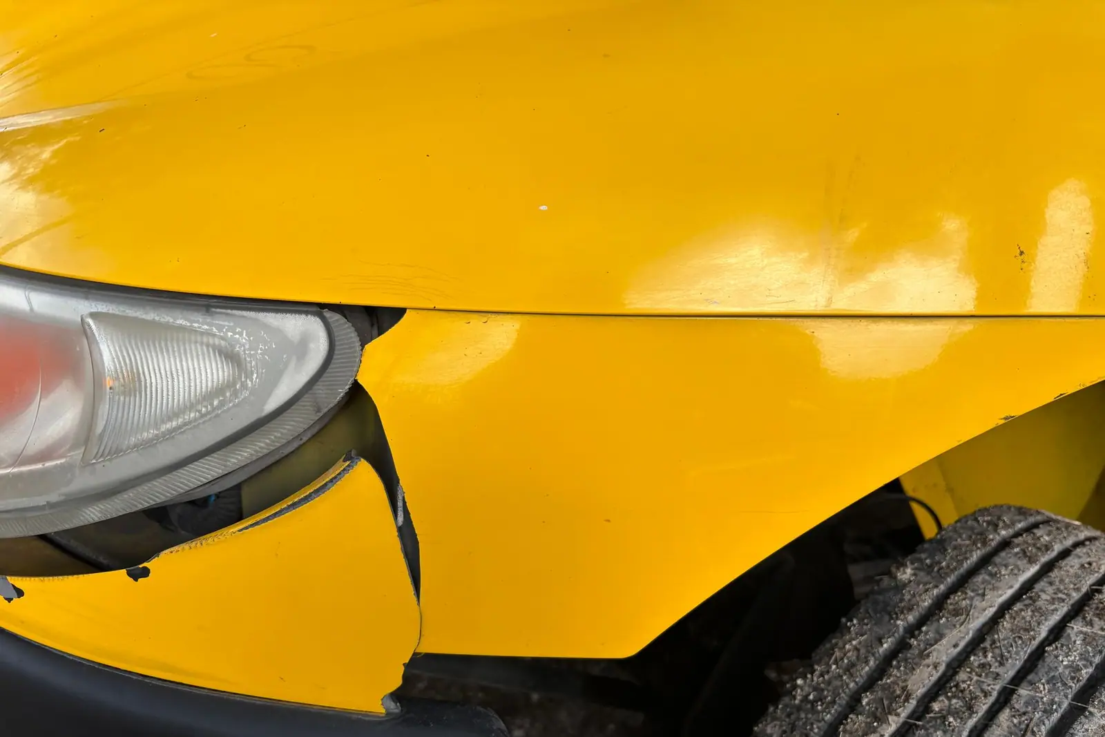 The front corner of a yellow car with a separated bumper and damaged bodywork