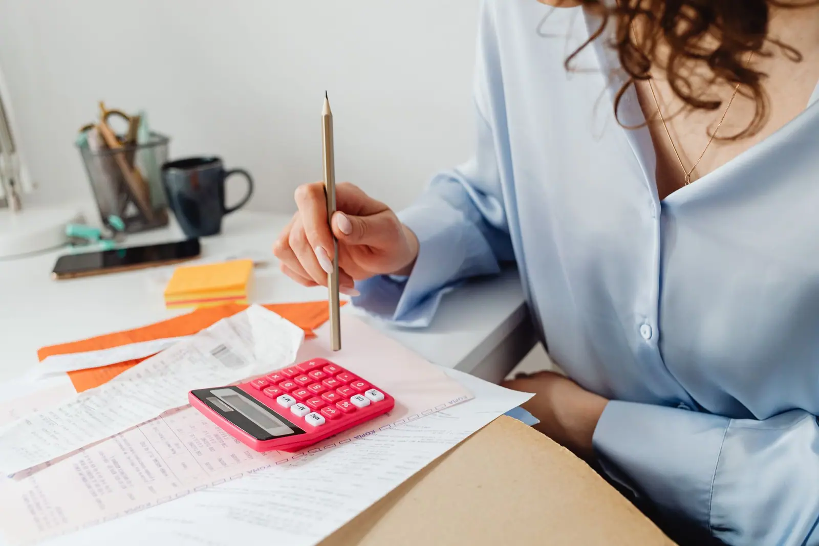 A person writing on paperwork beside a pink calculator