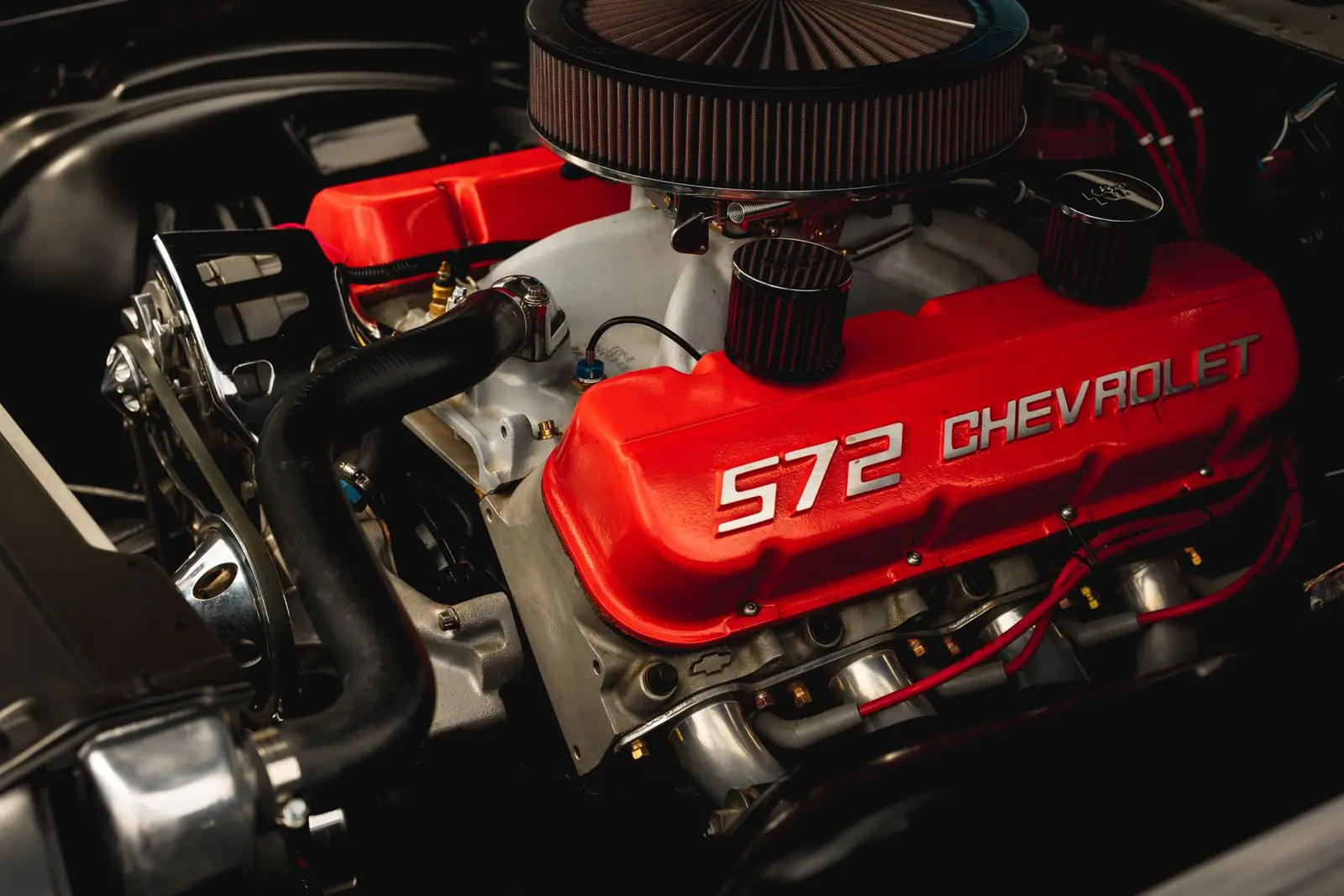 A round pleated air filter above a red engine cover marked 572 Chevrolet