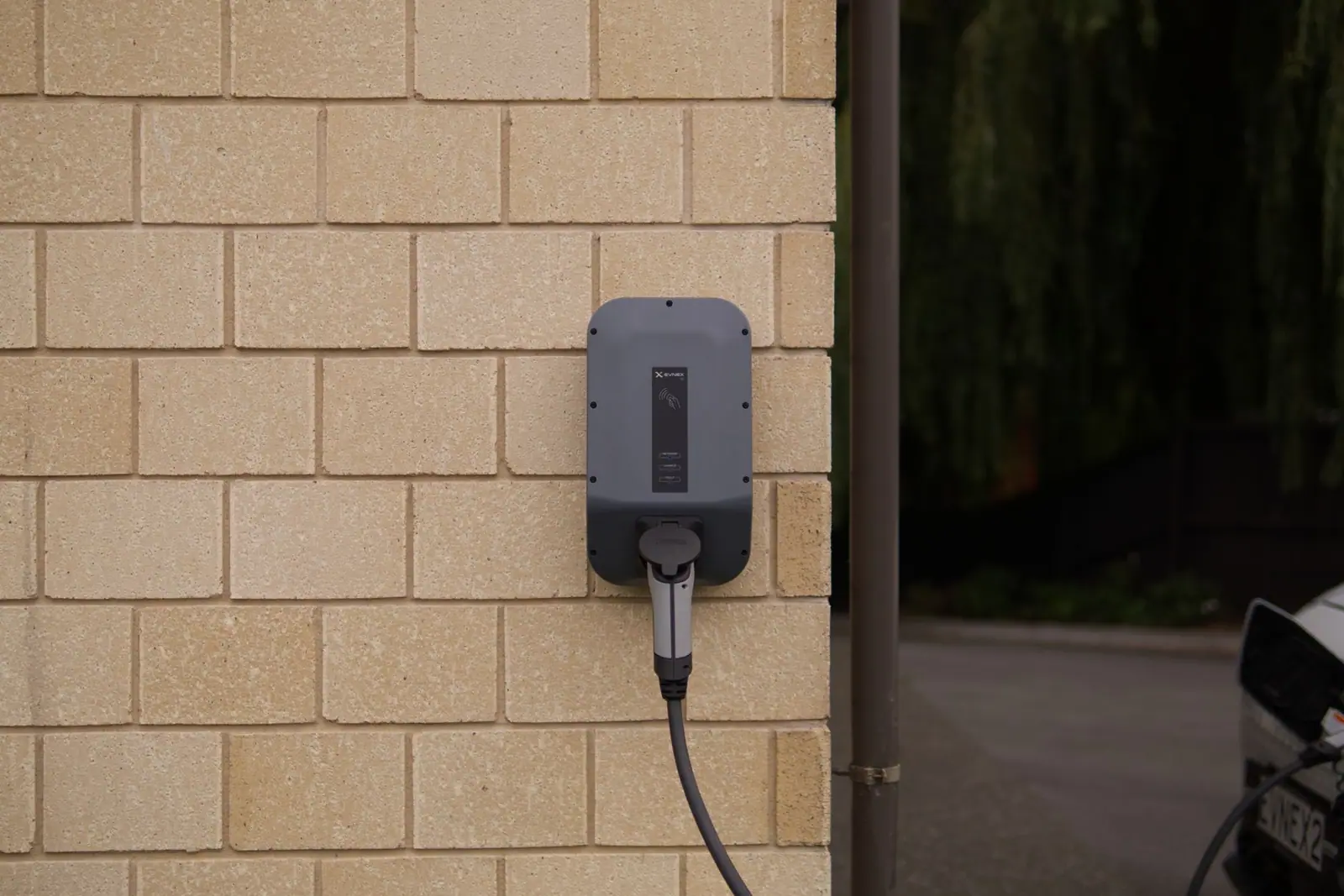 A dark gray wall-mounted EV charging unit on a pale brick wall