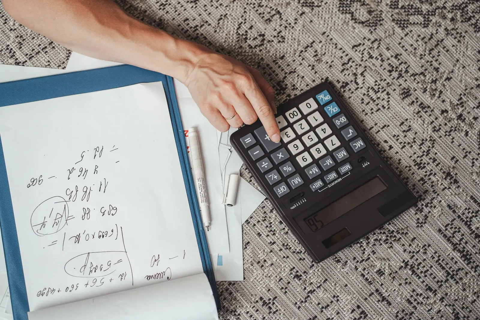 A hand using a calculator beside a notebook and papers