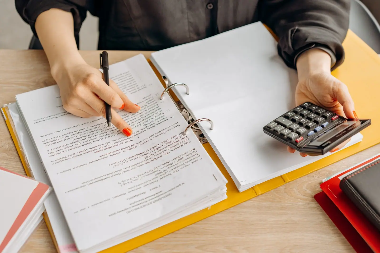 A person checking a document in a binder beside a calculator