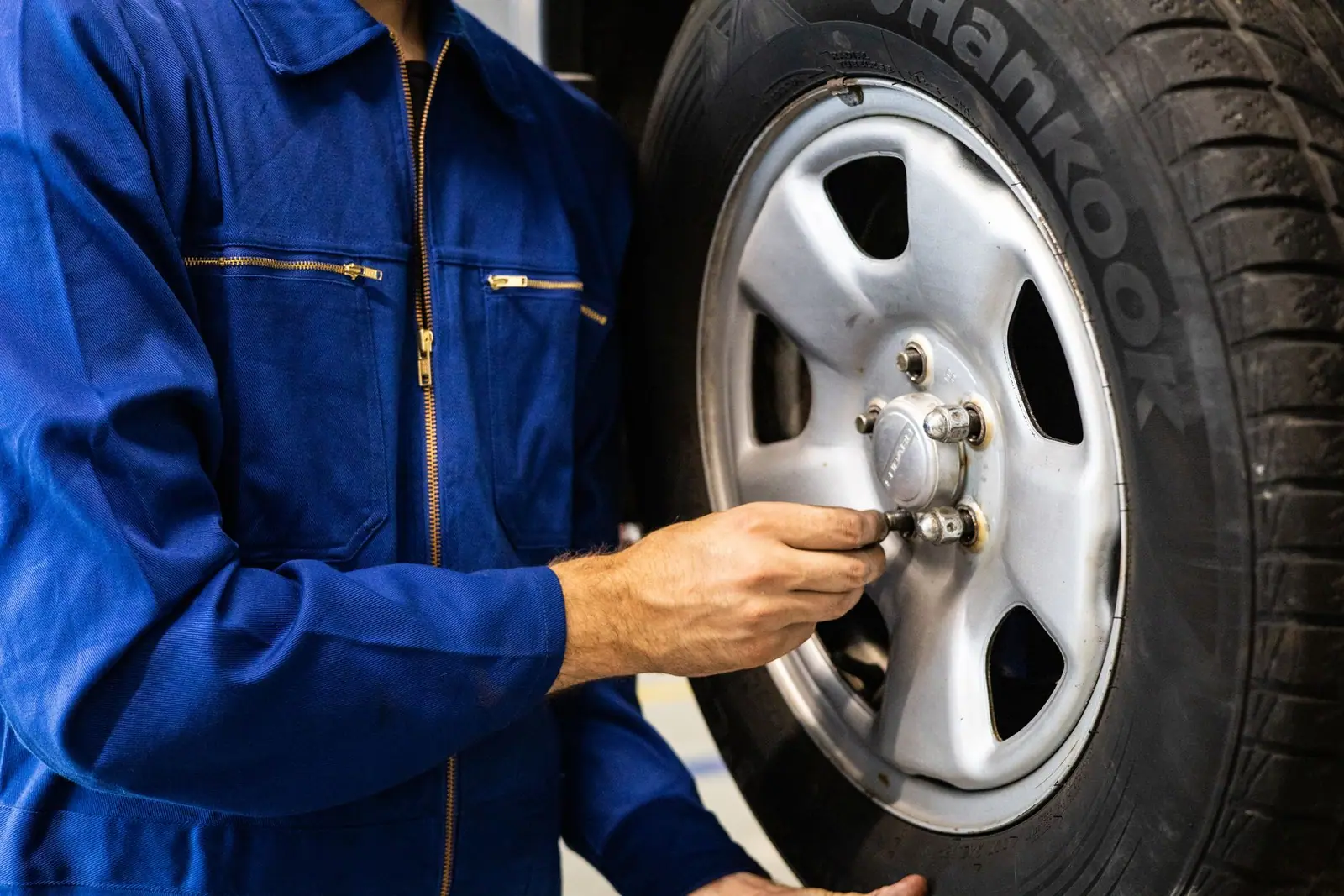 A mechanic in blue overalls inspecting a car tyre in a workshop