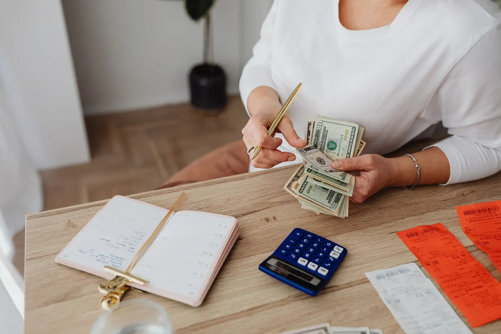 A woman counting dollar bills beside paperwork and a calculator at a table